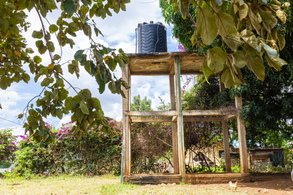 A black water tank sits on top of a concrete platform structure surrounded by trees and vegetation on a sunny day.