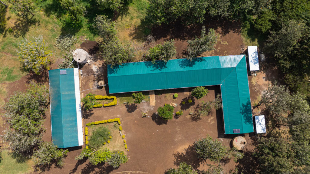 Aerial view of two L-shaped green-roofed buildings surrounded by trees, pathways, and landscaped garden areas.