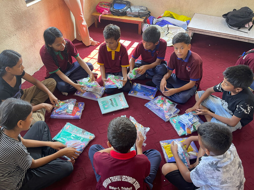 A group of children sitting in a circle on a red carpet, sorting and organizing small packages of school supplies.