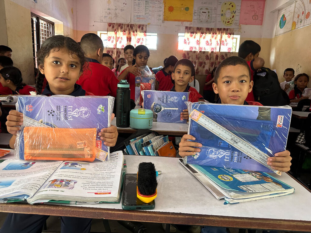 Two students holding new school notebooks and supplies at their desks in a classroom.