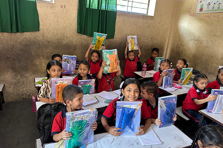 Primary school students in red and black uniforms sitting at desks holding new workbooks and notebooks.